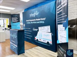 Trade show booth including a pop-up backwall, a counter in dye-sublimated fabric and 2 roll-up banner stands for the payment technologie company Checkflo.